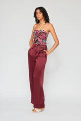 Woman wearing high-waisted, wide-leg silk purple trousers with a sleek, flowy silhouette, featuring gold accents and front pleats for a polished, comfortable look.