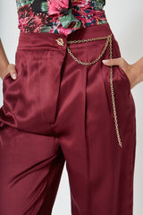 Woman wearing high-waisted, wide-leg silk purple trousers with a sleek, flowy silhouette, featuring gold accents and front pleats for a polished, comfortable look.