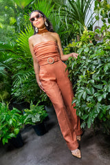 Full-length view of a model in a lush greenhouse path wearing the peach Bianca linen jumpsuit styled with tinted sunglasses and floral-embroidered heels.