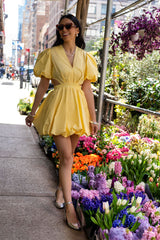 Model walking in the Cameron yellow bubble mini dress featuring puff sleeves, side cutouts, playful bubble skirt, and effortless style.