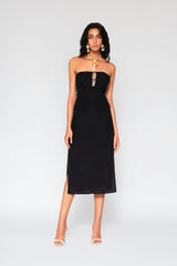 Full length studio portrait of a woman wearing the black Cate Halter Dress, featuring a ruched strapless bodice with a detailed corded halter neck ornament and side slit midi skirt.