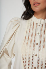Close up shot focusing on the high lace-trimmed collar, tortoiseshell buttons, and voluminous gathered puff sleeve of the ivory Eva cotton blouse.