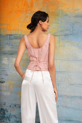 Rear view of a woman leaning against a multi-toned blue brick wall, showcasing the lace-up corset back closure of the red and white striped Ines bustier top.