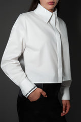 Three quarter studio view of a crisp white cotton button down shirt, emphasizing the clean hidden placket design and embroidered cuff detail.