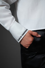 Close-up shot of a model with her hand in her black satin pants pocket, putting the embroidered white shirt cuff text in clear view.