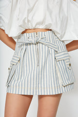 Close-up of the Mati Denim Skirt featuring front zipper, adjustable waist tie, cargo pockets, and blue stripe cotton denim fabric.