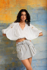 Mati Denim Skirt styled with a white blouse creates a modern resort look featuring blue stripes and utility inspired details.