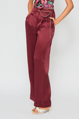 Woman wearing high-waisted, wide-leg silk purple trousers with a sleek, flowy silhouette, featuring gold accents and front pleats for a polished, comfortable look.