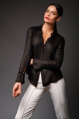 Studio portrait of a woman wearing the black Anita Silk Lurex Shirt with metallic gold pinstripes, featuring an unbuttoned collar and flared cuffs, paired with white trousers.