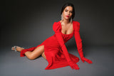 Glamorous studio editorial view of a model seated on the floor, showcasing the fluid drape of the red silk fabric, puff sleeves, and matching opera gloves.