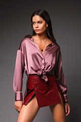 Three-quarter portrait of a woman showing how the mauve silk Daisy blouse can be styled with an adjustable front-knot tie at the waist, emphasizing its fluid satin drape.