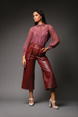 Full length studio portrait of a woman modeling the mauve pink Martha Sheer Lace Blouse with pleated bishop sleeves, styled with high waisted burgundy faux leather culottes and cream platform heels.