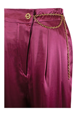 Woman wearing high-waisted, wide-leg silk purple trousers with a sleek, flowy silhouette, featuring gold accents and front pleats for a polished, comfortable look.