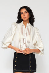 Three-quarter studio portrait of a model showcasing the sheer open-work lace panels running down the bodice of the ivory Eva cotton blouse.