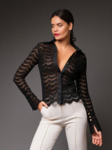 Three-quarter studio portrait focusing on the front details of the black Joan sheer lace shirt, displaying its open collar styling and delicate gold buttons on the wrist of the sleeve.