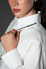Close up shot focusing on the collar of a white poplin cotton shirt, highlighting the black embroidered text that reads "MADE BY IMMIGRANTS".