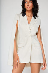 Three-quarter close-up portrait of the ivory Michelle cape blazer dress, highlighting the tailored front flap pockets and the sharp contrast of the black satin collar against the white fabric.