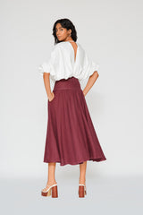 Rear studio perspective of a model showcasing the high-waisted flared yoke silhouette and clean back construction of the burgundy Patricia linen midi skirt.