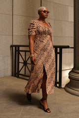 Full-length street style portrait of a woman wearing the leopard print Sandra Maxi Dress, showcasing its structured milkmaid-style bodice, high front slit, and short puff sleeves.