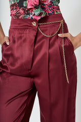 Close up photo of woman wearing high-waisted, wide-leg silk purple trousers with a sleek, flowy silhouette, featuring gold accents and front pleats for a polished, comfortable look.