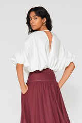 Rear studio shot of a model showing the deep V-shaped open back and gathered elastic waist structure of the white Zoila cotton top.