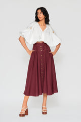 Full-length studio image of a woman modeling the white cropped Zoila cotton top, styled with a high-waisted button-front burgundy maxi skirt and white platform sandals.