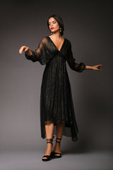 Full-length studio portrait of a woman wearing the black Paula dress, showcasing its fluid metallic gold pinstripe chiffon, deep V-neckline, and sheer batwing sleeves.