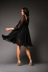 Rear studio perspective of a model glancing over her shoulder, highlighting the dramatic volume, high neck tie closure, and layered movement of the black chiffon Penelope mini dress.